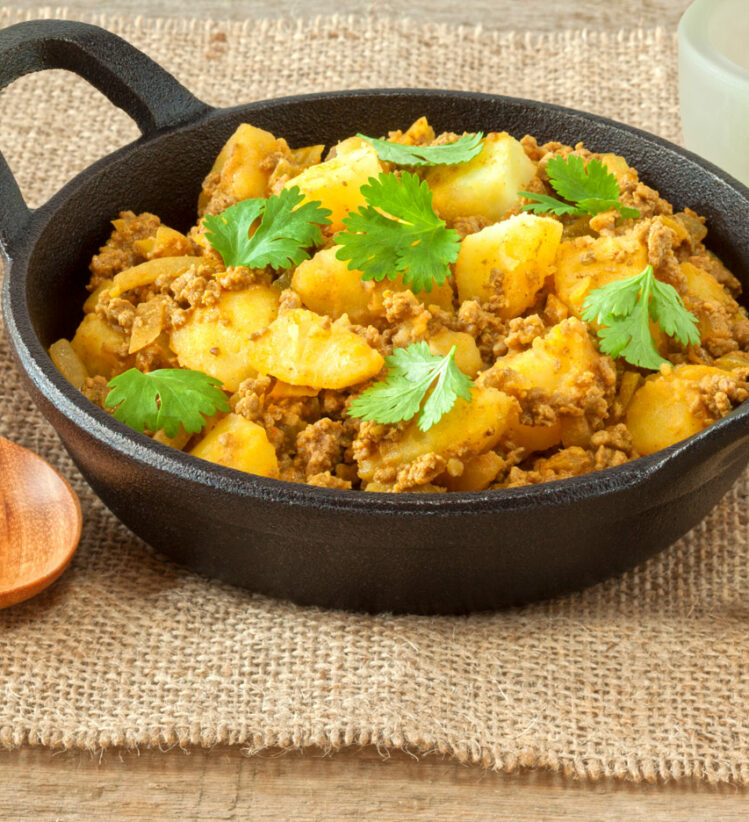 Aloo keema served in a cast iron dish with a wooden spoon