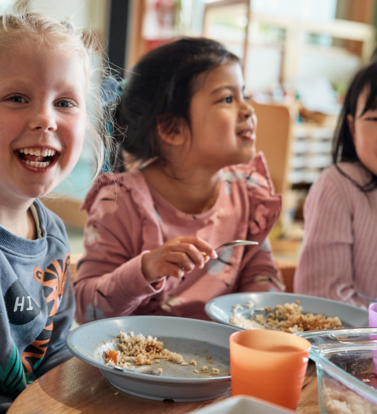3 kids in a early childhood centre eating lunch around a table.