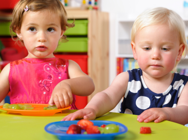 Two little kids at a childcare centre with a plate of fruit
