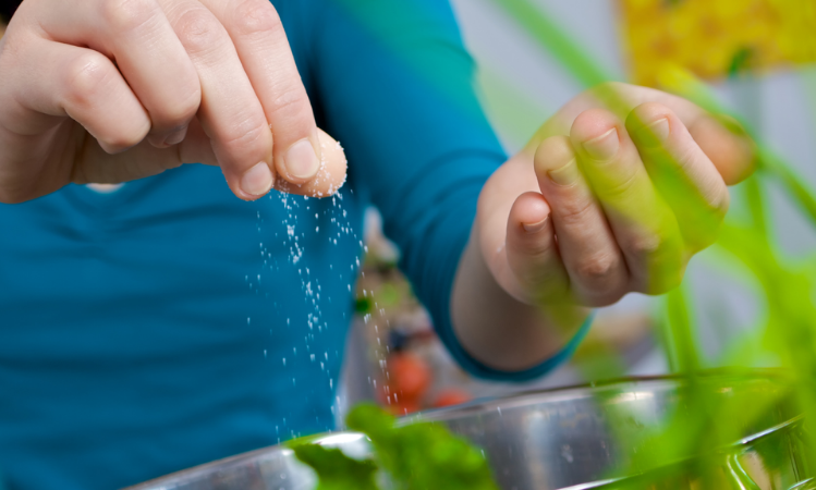 A person with a pinch of salt adding to a bowl