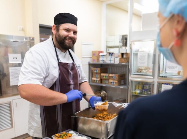 Smiling chef serving food into a plastic container