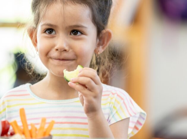 Child smiling and eating a vegetable