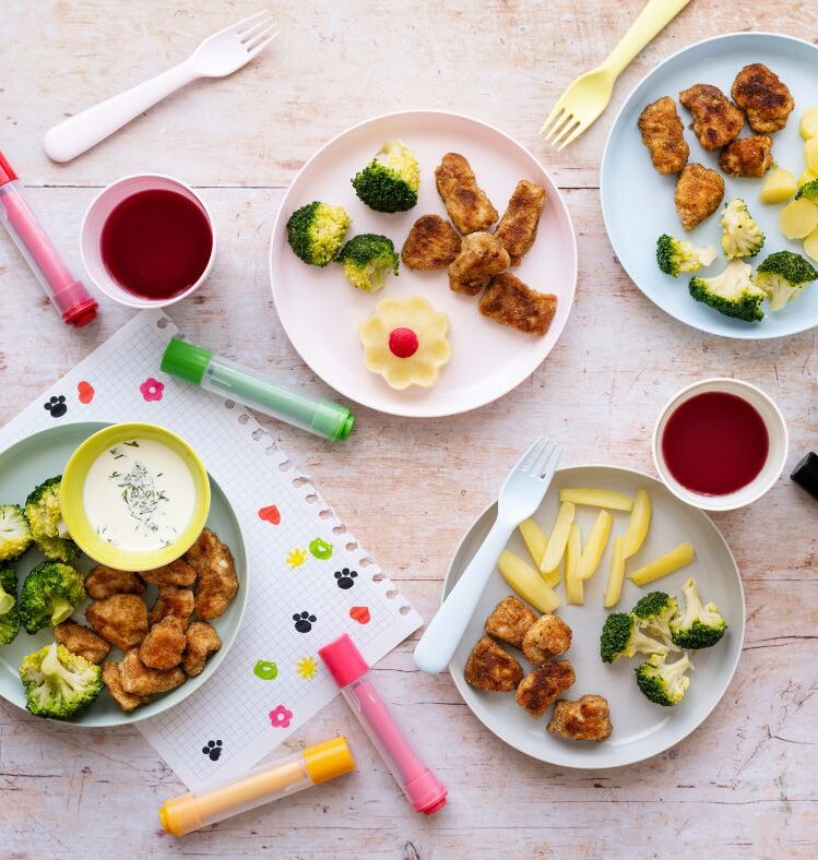 Children's meals on plates with art materials and paper scattered around