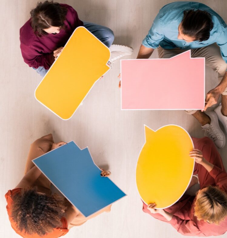 four people facing each other holding signs shaped like speech bubbles