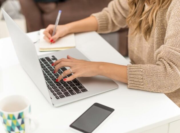 a person using a laptop and writing notes in a book