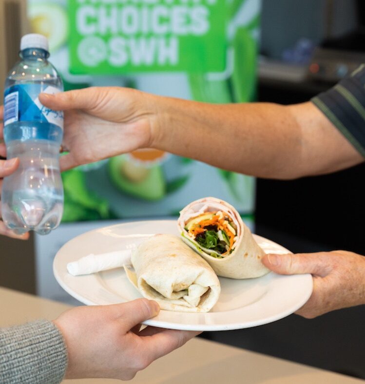 Woman handing over a wrap on a plate and a bottle of water to a customer