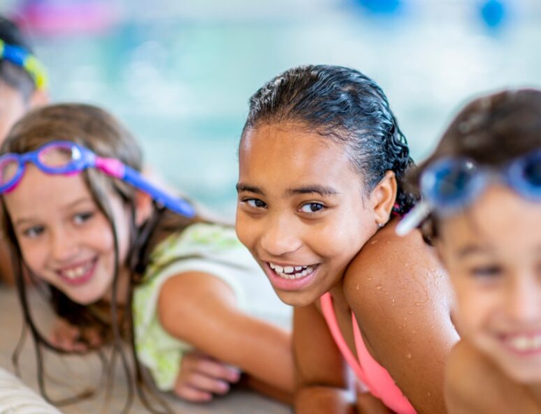 Group of children lined up on the edge of a swimming pool smiling