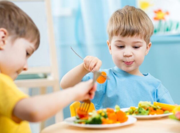 Two boys at a table eating vegetables