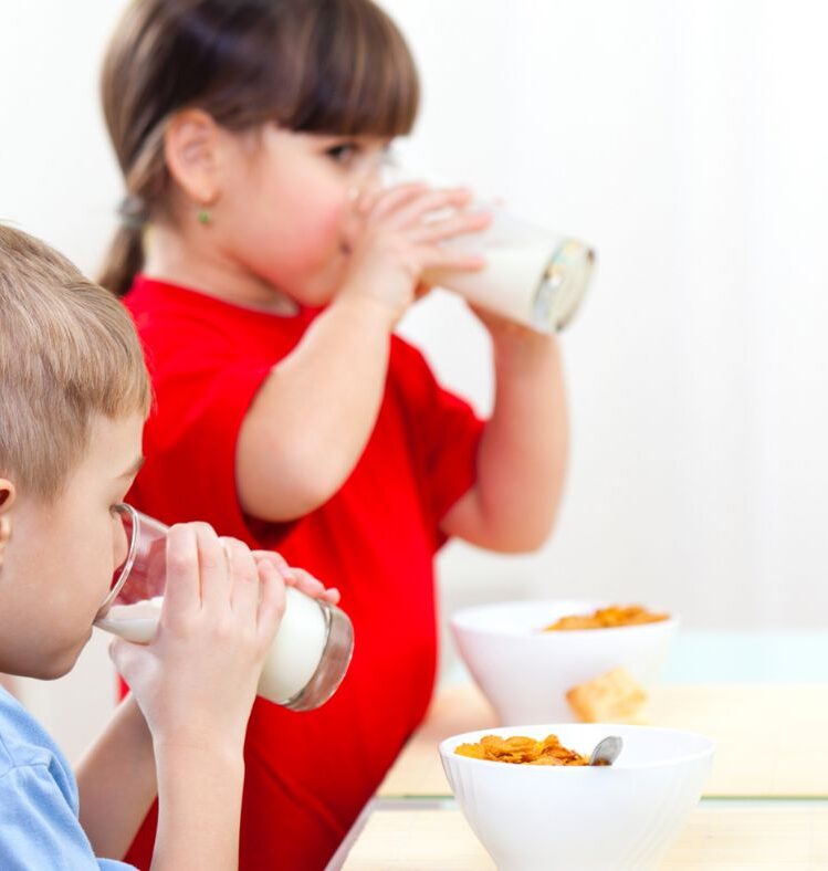 Two children drinking milk with bowls of cereal