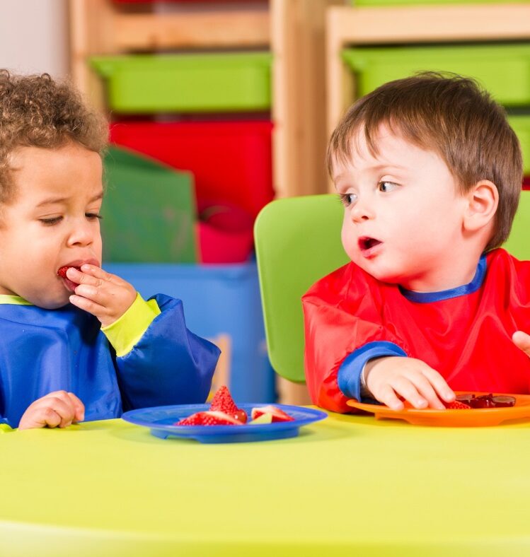 Two young boys eating fruit off plates at a yellow table