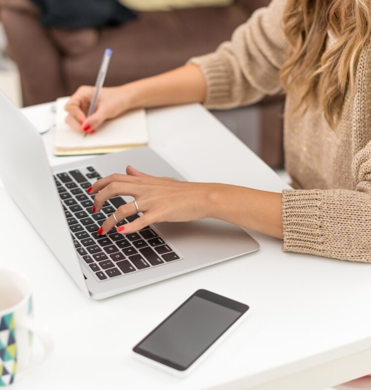 Woman working on a laptop and writing on a note pad
