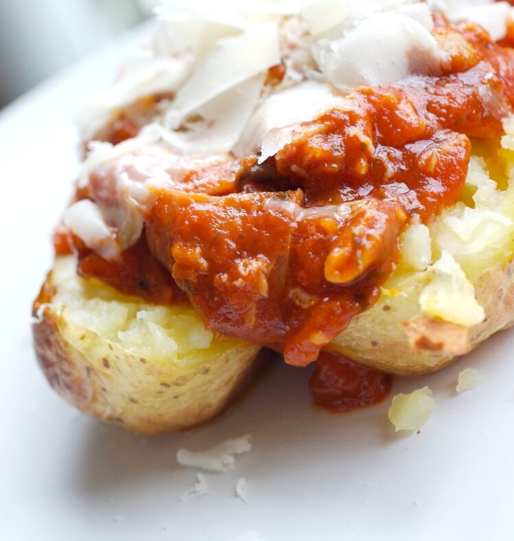 A baked potato sliced vertically in half topped with bolognaise and cheese