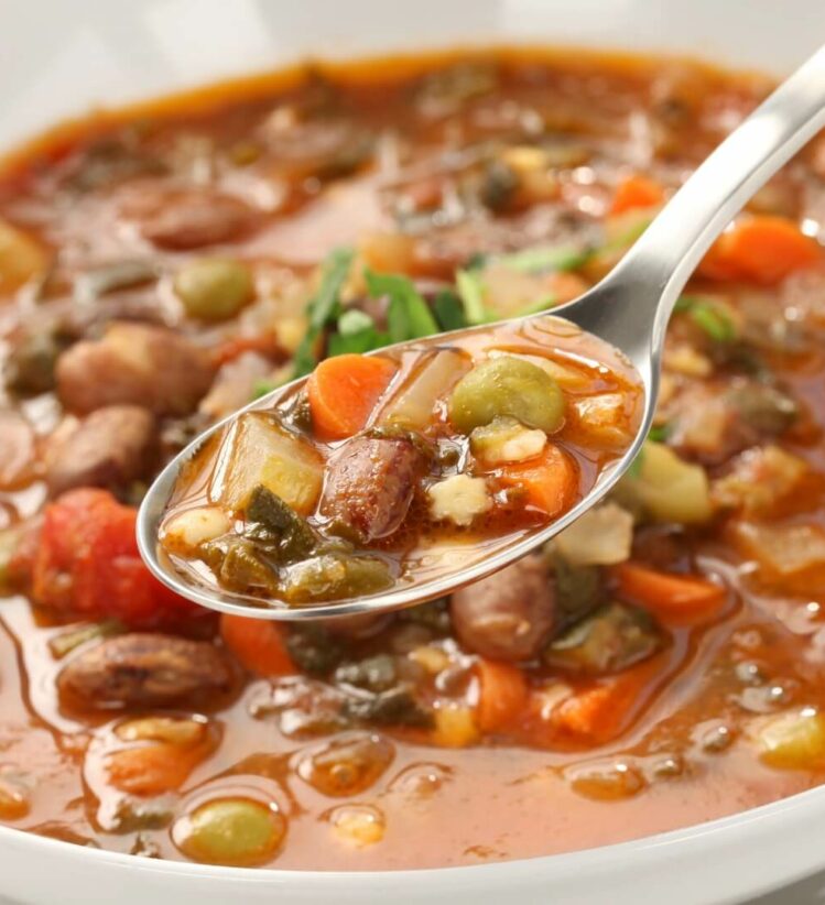 a spoonful of minestrone soup above a bowl of soup