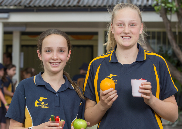 Students smiling at the camera with some fruit in their hands