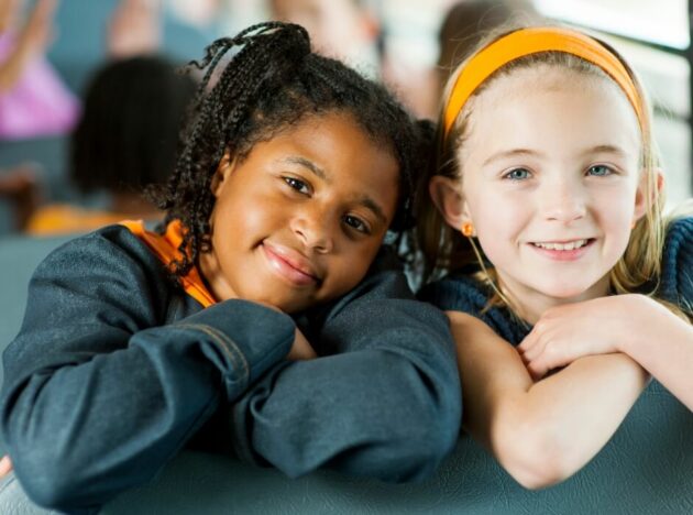two children smiling next to each other on a school bus