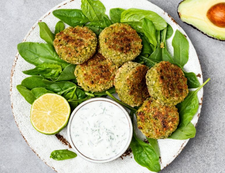 Falafel balls on a bed of lettuce with a slice of lemon and a small dish of tzatziki dip.