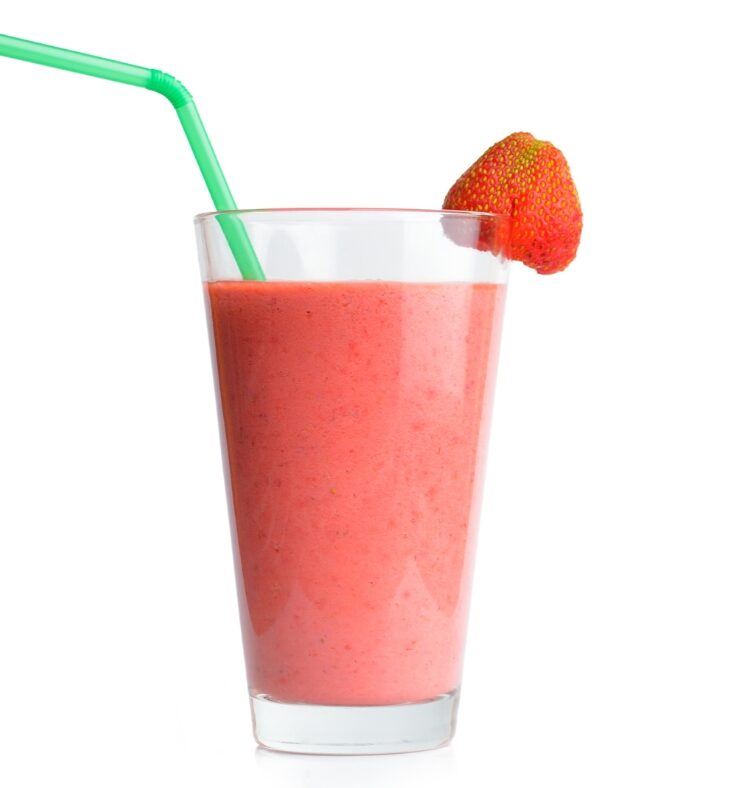 Glass filled with a red smoothie, with a green straw in it and a strawberry on the rim