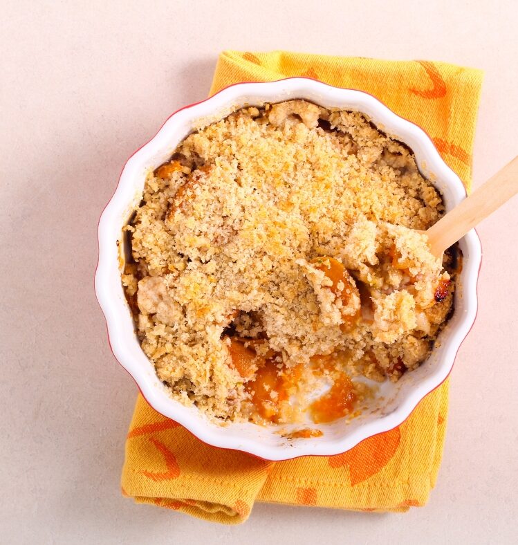 Fruit crumble in a white bowl with a wooden spoon lifting some out