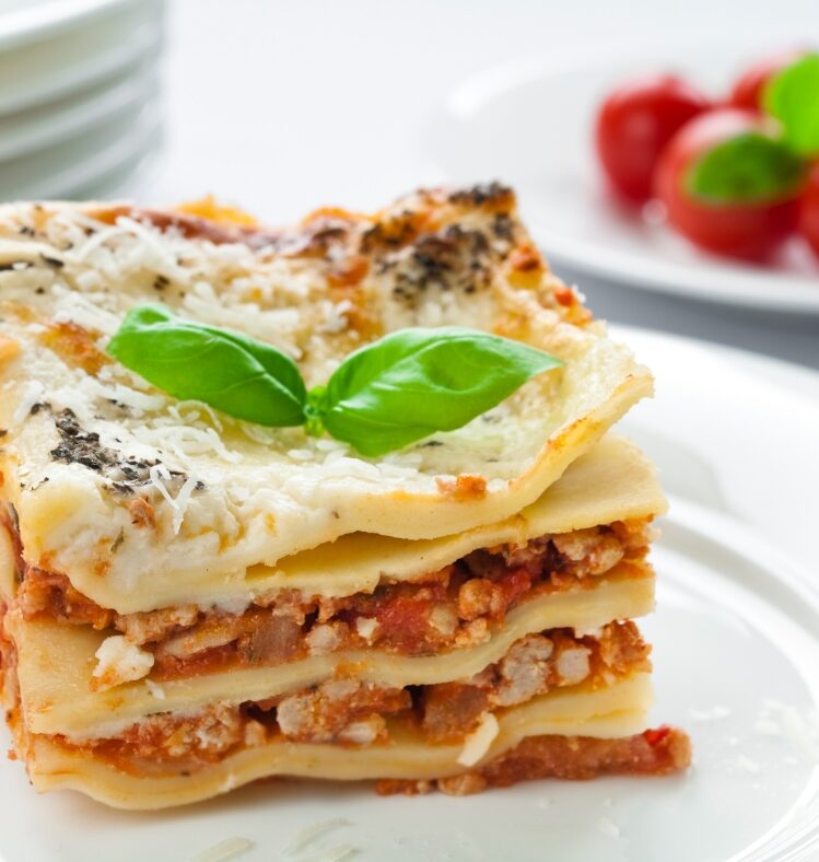 A square slice of lasagne on a plate with two green herb leaves on top