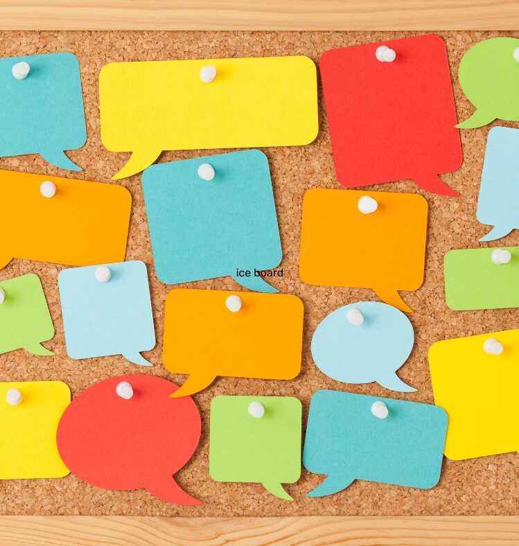A cork pinboard with lots of different coloured paper speech bubbles pinned to it