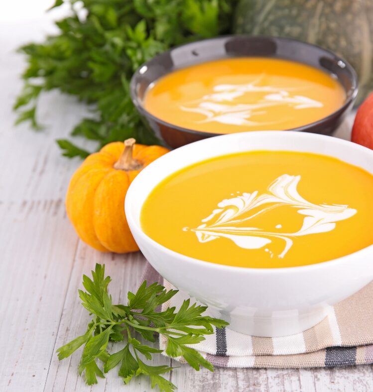 Two white bowls containing pumpkin soup, on a tea towel
