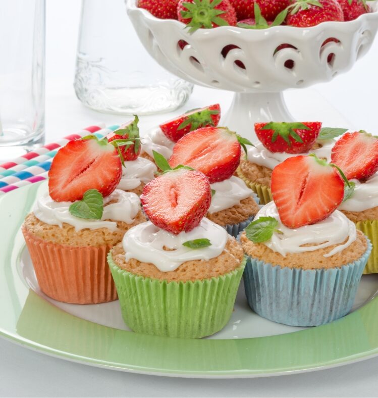 A plate full of muffins with white icing and sliced strawberries on top