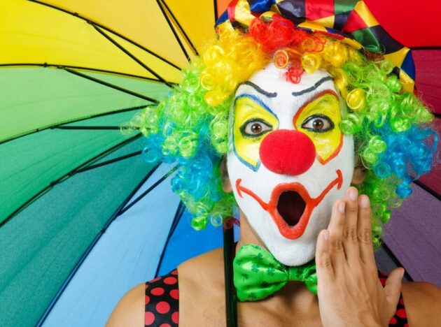 a suprised clown holding a rainbow umbrella