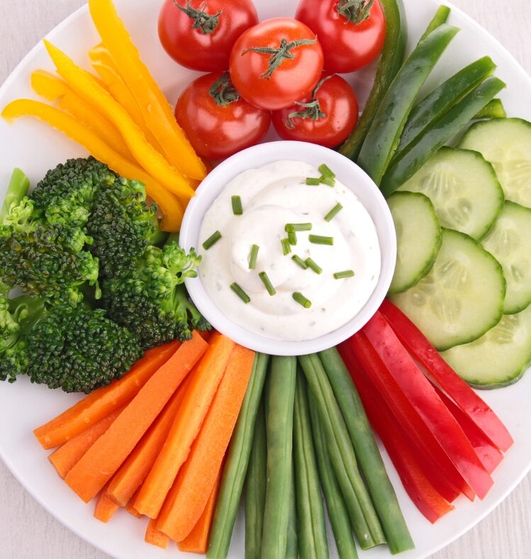 a small bowl filled with tzatziki dip surrounded by various sliced vegetables