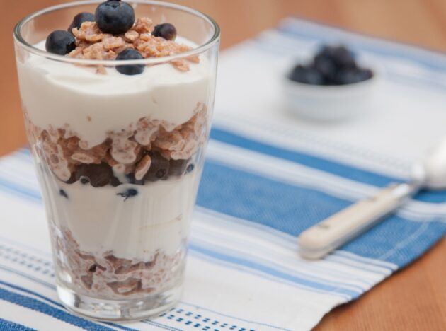 A glass with layered yoghurt, cereal and blueberries