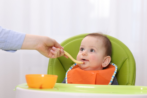 Baby in a high chair being fed pureed food