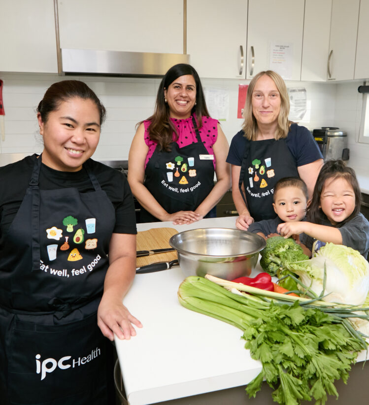 3 cooks in a kitchen with aprons, with two kids smiling and touching food